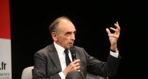 Eric Zemmour durante discurso, sentado, segurando o microfone