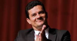 Foto de Sérgio Moro sorrindo, batendo palmas, fundovermelho desfocado