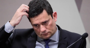 Foto de Sergio Moro com a cabeça baixa, olhar preocupado e mão direita coçando o cabelo na lateral.