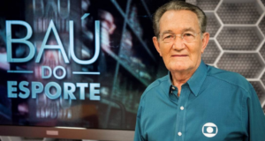 Foto de Léo Batista com cabelos grisalhos, usando óculos e camisa ao azul. No lado esquerda imagem tem "Baú do Esporte", quadro do programa Globo Esporte que ele apresentava