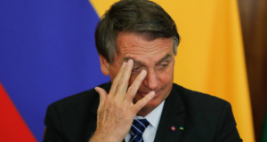 Foto de Bolsonaro com a cabeça abaixada e mão direita na testa.