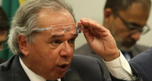 Paulo Guedes recebe carta de funcionários por reajuste. Ele tem o óculos levantado dos olhos e expressão de susto.