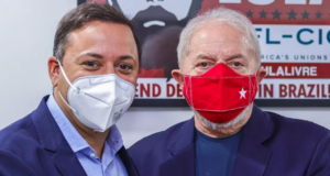 Foto de Andre Cecliano e o ex-presidente Lula. Ambos usam ternos azuis, usam máscara. Ceciliano tem cabelo castanho e pele branca.