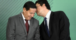 Moro se derrete por Mourão: "Voz sensata na República". Moro fala ao ouvido de Mourão, ele usa terno preto e Mourão terno cinza.