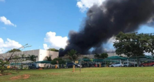 Garagem do Palácio do Planalto pega fogo. Foto de fumaça preta subindo no céu com estrutura do galpão ao fundo.