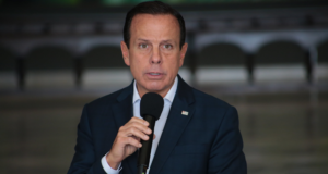 Nanico nas pesquisas, Doria chama de "golpista" quem quer tirá-lo da disputa. João Doria tem expressão de desânimo enquanto fala ao microfone. Ele está vestindo um terno azul marinho.