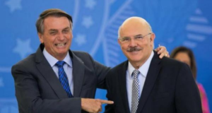 Em live, Bolsonaro diz que bota "a cara no fogo" por Milton Ribeiro. Foto do presidente Bolsonaro apontando o dedo e sorrindo para Milton Ribeiro.