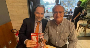 Alckmin posta foto segurando livro sobre Lula. Foto de Alckmin sorrindo em uma mesa ao lado de um advogado do grupo Prerrogativas, que segur ao livor.