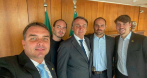 Imagem do presidente Bolsonaro junto com os filhos. Eles estão um ao lado do outro e sorriem para uma selfie.