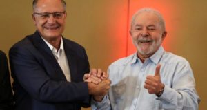 Foto de Lula sorrindo ao lado de Geraldo alckmin. Os dois estão dando um aperto de mãos.