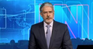 William Bonner usa terno preto, gravata, barba e cabelos grisalhos. Ele está no estúdio do Jornal Nacional.