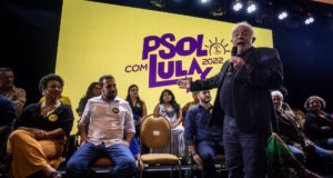 Foto do ex-presidente Lula falando em um palanque com o símbolo do PSOL ao fundo.