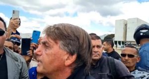 Foto de Bolsonaro falando a apoiadores, ele usa roupa preta, tem cabelo grisalho, pele branca e expressão de intimidação.