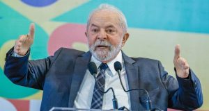 Lula em foto de roupa social, falando em microfone e gesticulando com os braços