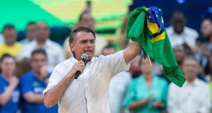 Jair Bolsonaro de camisa branca e segurando bandeira do Brasil