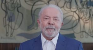 Lula falando para a câmera, com camisa branca e paletó azul