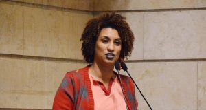 Marielle Franco falando em microfone, com roupa colorida