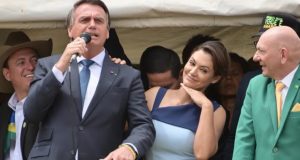 Jair Bolsonaro falando em microfone, perto de Michelle Bolsonaro e Luciano Hang