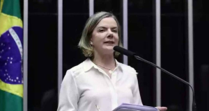 Gleisi Hoffmann de roupa branca, falando em microfone e segurando papel