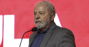 Lula com expressão séria, olhando para o lado, em fundo vermelho