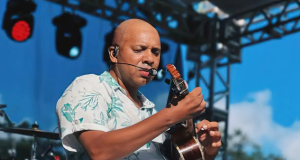 Anderson Leonardo cantando e tocando cavaquinho, com camisa estampada azul e branca