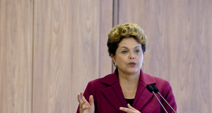 Dilma Rousseff falando e gesticulando com roupa cor de vinho