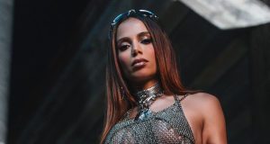 Anitta com roupa prateada e óculos escuros na cabeça, fazendo carão para foto