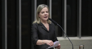 Gleisi Hoffmann de roupa preta, em pé, falando em microfone e segurando papel, na Câmara dos Deputados