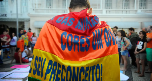 Pessoa com bandeira contra o preconceito, de costas, perto de multidão