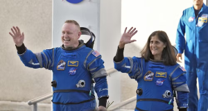 Butch Wilmore e Suni Williams, astronautas da Nasa, de uniforme, acenando e sorrindo sem olhar pra câmera