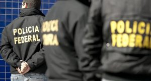 Três agentes da Polícia Federal uniformizados, de costas, lado a lado