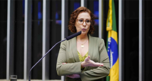 Deputada federal Carla Zambelli (PL-SP) de roupa verde e amarela, em pé, falando em microfone e gesticulando