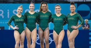 Flávia Saraiva, Julia Soares, Rebeca Andrade, Jade Barbosa e Lorrane Oliveira sorrindo, lado a lado, com uniforme