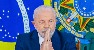 Lula com bandeiras ao fundo, mãos unidas e expressão séria