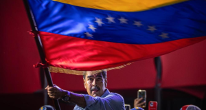 Nicolás Maduro sério, balançando bandeira da Venezuela