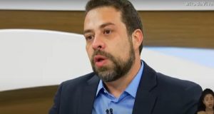 Guilherme Boulos de roupa social azul, sem olhar para a câmera, falando, no Roda Viva