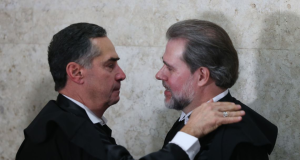 Luís Roberto Barroso e Dias Toffoli de perfil, sérios, se cumprimentando e se olhando, ambos de preto