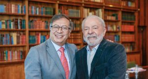 Gustavo Petro e Lula em aperto de mãos, sorrindo e posando para foto com estantes de livros ao fundo