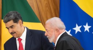 Nicolás Maduro, presidente da Venezuela, e Lula, caminhando, sérios, lado a lado, com bandeiras ao fundo