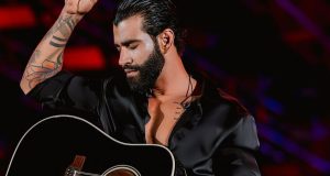 Gusttavo Lima com roupa e violão preto, de olhos fechados em show