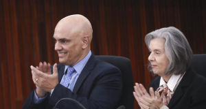 Alexandre de Moraes e Cármen Lúcia de perfil, sorrindo e batendo palmas